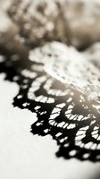 Delicate lace fabric casting intricate shadow patterns on white surface in soft natural light creating elegant contrast for fashion and textile design projects.