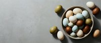 Colorful Easter eggs in neutral tones arranged in wooden bowl on gray textured surface with scattered eggs creating festive holiday decoration.