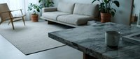 Modern minimalist living room interior with dark marble coffee table, gray sofa, wooden chair and green plants creating cozy Scandinavian home decor atmosphere.