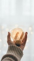 Hand holding glowing light bulb with warm illumination against soft bokeh background representing innovation, creativity and bright ideas for business solutions.