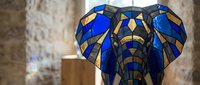 Stained glass elephant head sculpture with vibrant blue and amber geometric patterns displayed in modern interior setting for decorative art projects.