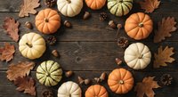 Autumn pumpkins arranged in circle with fall leaves, acorns and pine cones on rustic wooden background for seasonal decoration and harvest celebration.