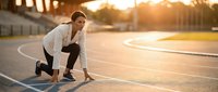 Young athletic woman in starting position on running track during golden hour sunset preparing for sprint race at outdoor stadium.