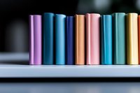 Colorful battery cells arranged in row on light surface showing variety of metallic pastel colors, selective focus with blurred background for technology design.