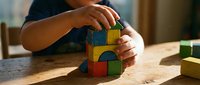 Child hands playing with colorful wooden building blocks on table in warm sunlight creating educational development activity for learning and creativity.