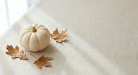 White pumpkin with autumn maple leaves on neutral fabric background. Seasonal fall decoration for harvest festival, thanksgiving crafts and holiday design projects.
