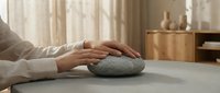 Hands gently touching smooth stone for meditation and mindfulness practice in serene home interior with natural lighting and wooden furniture.