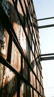 Weathered brick industrial building facade with rusted metal fire escape and horizontal steel beams against overcast sky, suitable for urban architecture and industrial design projects.