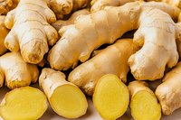 Fresh ginger root rhizomes whole and sliced showing yellow flesh interior, close up macro shot on white background for cooking and health benefits.