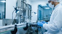 Scientist in white lab coat and protective mask operating advanced pharmaceutical or biotechnology equipment in sterile laboratory setting, conducting research or quality control testing.