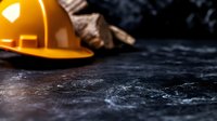 Orange construction hard hat on dark textured concrete surface with dramatic lighting and copy space, safety equipment concept for construction industry.