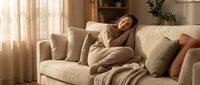 Young woman in beige sweater relaxing on comfortable sofa at home, enjoying peaceful moment in cozy living room with warm natural lighting.
