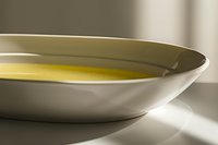 White ceramic plate with golden olive oil creating smooth reflective surface in natural sunlight, minimalist food photography composition for culinary and restaurant use.