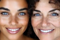 Close up portrait of young and mature women with bright blue eyes, freckles, and natural curly hair showing genuine smiles and aging comparison.