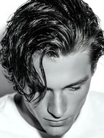 Black and white portrait of young man with wet, styled hair looking down, creating dramatic shadows on face. Ideal for fashion and beauty advertising.