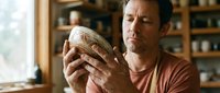 Middle-aged Caucasian man examining handcrafted ceramic bowl in rustic kitchen setting. Artisan pottery appreciation and craftsmanship evaluation concept.