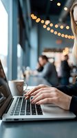 Young woman working on laptop in cozy cafe with warm string lights and coffee cup creating productive remote work atmosphere for freelancers and entrepreneurs.