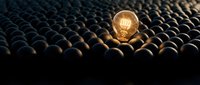 Glowing incandescent light bulb standing out among dark unlit bulbs, symbolizing innovation, creativity, unique ideas, and competitive advantage in business and technology concepts.