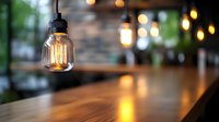 Vintage Edison bulb hanging from black cord above wooden table with warm bokeh lights and brick wall background.