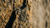 Rough textured stone wall surface with natural weathered patterns and deep shadows creating dramatic contrast for architectural backgrounds.