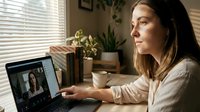 Young professional woman having video conference call on laptop at home office desk with plants and natural lighting for remote work communication.