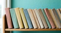 Row of vintage books with colorful spines arranged on wooden shelf against turquoise wall for home decor, education, and reading concepts.