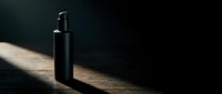 Black pump bottle with spray dispenser on wooden surface with dramatic lighting and dark background, suitable for cosmetics, skincare, and product packaging design.