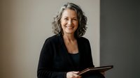 Confident mature businesswoman with gray hair smiling while holding tablet in modern office setting for corporate presentations and professional marketing.