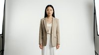 Young East Asian woman in professional beige blazer and white dress standing against white background, suitable for corporate, business, and fashion design projects.