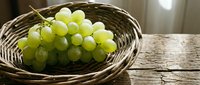 Green grapes in wicker basket on wooden table, fresh fruit produce for healthy eating, cooking, nutrition, and food styling projects.