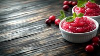 Fresh cranberry sauce with whole berries and mint leaves in white ramekins on rustic wooden background, selective focus with copy space for text.