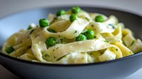 Creamy fettuccine pasta with fresh green peas and herbs in dark ceramic bowl, close-up view of homemade Italian cuisine served for lunch or dinner.