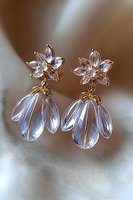 Elegant crystal flower drop earrings with gold details on soft blurred background. Delicate floral studs feature translucent petals and dangle elements for bridal jewelry.