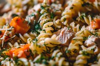 Fusilli pasta salad with tuna chunks, fresh cherry tomatoes and aromatic herbs in close up view, selective focus on pasta spirals and colorful ingredients.
