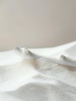 Soft white cotton fabric with gentle folds and natural shadows creating minimalist texture, suitable for lifestyle and fashion photography backgrounds.