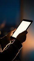 Hands holding a tablet with glowing blank screen in dark ambient light, warm bokeh background, mockup ready for app or web design.
