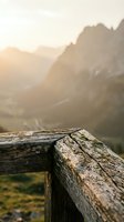 Weathered wooden railing in sharp focus with misty mountain valley and golden sunrise light in soft-focus background, capturing serene alpine landscape scenery.