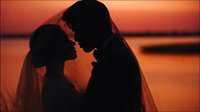 Romantic couple silhouette at sunset by water, intimate moment between bride and groom during golden hour, wedding photography concept for love and marriage.