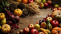 Autumn harvest arrangement with pumpkins, apples, cranberries, wheat stalks and seasonal vegetables on rustic wooden background for thanksgiving decor.