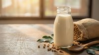 Fresh soy milk in glass bottle with soybeans spilling from burlap sack on rustic wooden table. Healthy plant-based dairy alternative for breakfast and cooking.