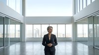 Middle-aged man in dark business suit standing in modern empty office space with floor-to-ceiling windows overlooking city skyline, corporate workspace concept.