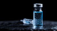 Medical vial with blue liquid and syringe on dark background, dramatic lighting highlights bubbles in transparent solution for healthcare concept.