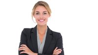 Young professional woman in black blazer and gray blouse smiling confidently with arms crossed, representing business leadership and success in corporate environment.