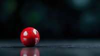 Vibrant red glossy sphere on dark reflective surface with blurred background creates dramatic minimalist composition highlighting shape and color contrast.