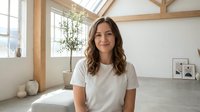 Young brunette woman in white t-shirt smiling in bright modern loft apartment with wooden beams and large windows for lifestyle and home concepts.