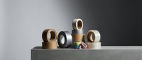 Assorted adhesive tape rolls in neutral colors arranged on concrete surface for packaging and shipping applications in modern minimalist setting.