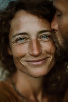 Close-up portrait of smiling middle-aged Caucasian woman with freckles and curly brown hair showing genuine happiness and natural beauty in warm lighting.