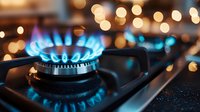 Blue gas flame burning on modern kitchen stove with bokeh lights in background, close up view showing energy consumption and cooking concept.