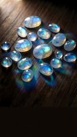 Collection of rainbow moonstone cabochons with iridescent blue flash scattered on dark wooden surface for jewelry making and gemstone crafts.