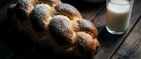 Fresh baked challah bread with poppy seeds on rustic wooden table next to glass of milk for traditional Jewish Sabbath breakfast or holiday meal.